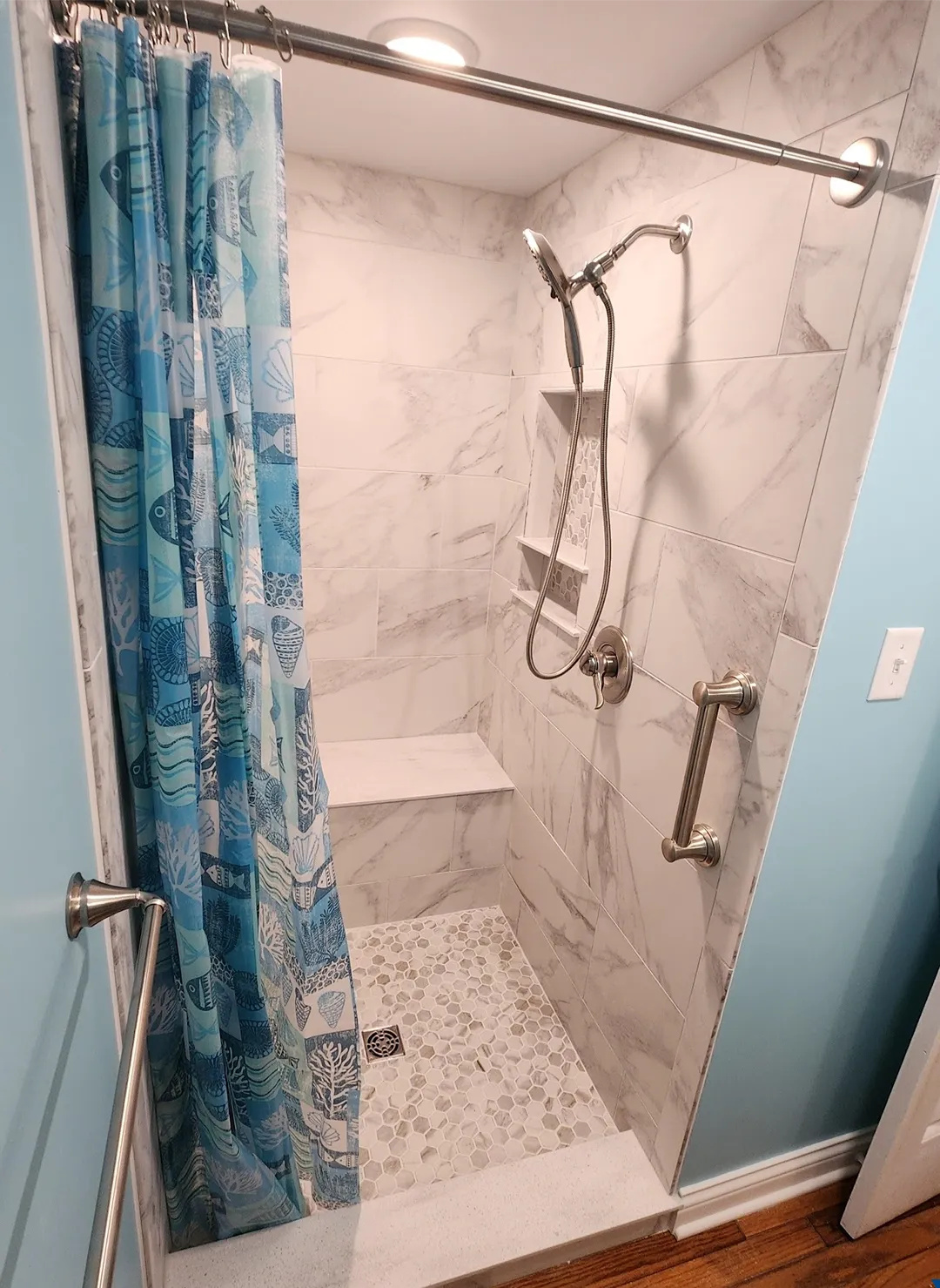 Walk-in shower with large marble-look wall tile, a built-in bench and niche, and a small pebble-style mosaic floor