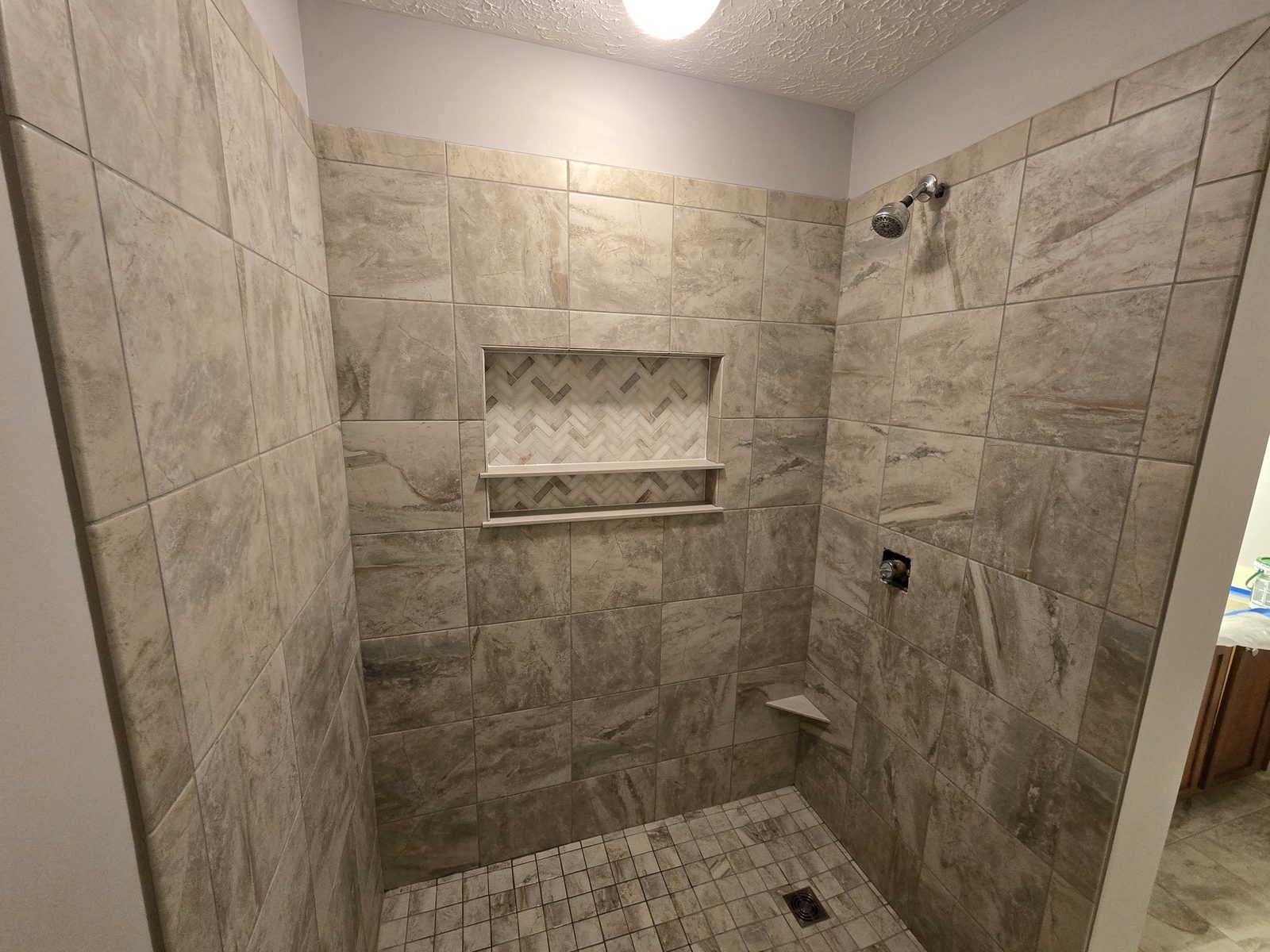 Gray porcelain shower walls and herringbone niche with a chrome shower head in Lafayette