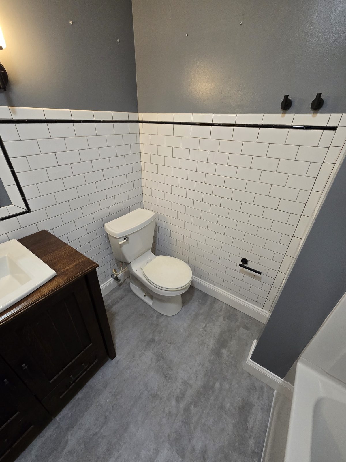 Existing white subway tile wainscoting preserved beside new gray vinyl plank flooring