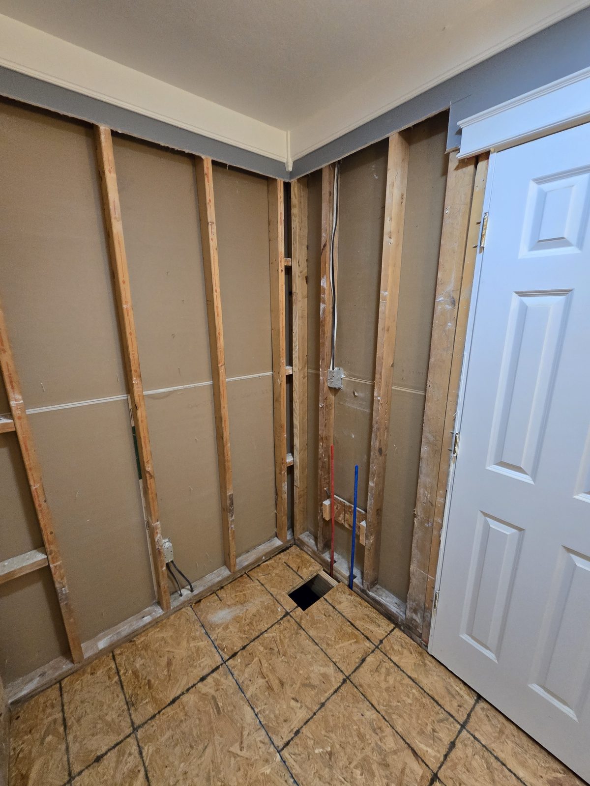 Wall framing opened for plumbing beside the new subfloor in West Lafayette